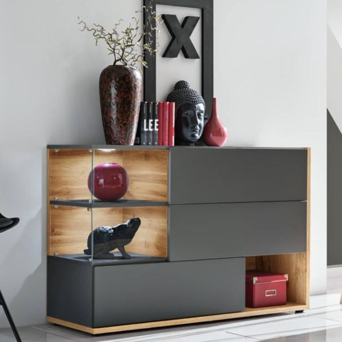 A modern sideboard cabinet with a mix of closed and open compartments, finished with LED lighting, in a pearl grey color, with decorative items displayed on top.