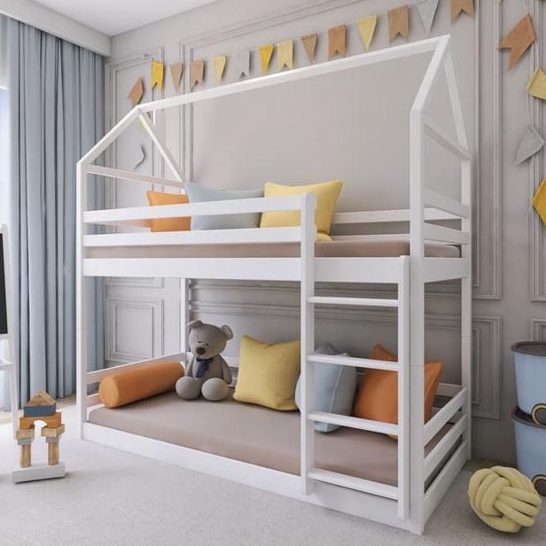 White children's house-shaped bed with colorful pillows and a teddy bear in a room.