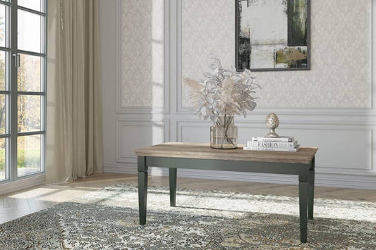 A rectangular coffee table with a green base and Oak Lefkas wooden top, placed on a patterned rug. The table is accompanied by decorative items and placed against a wall with a window, showcasing a room with elegant interior decor.