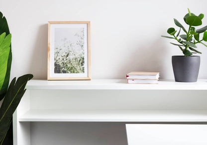 White desk with a framed picture, books, and a plant on a light background