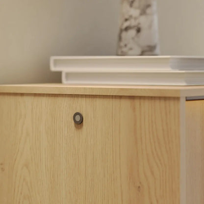 Wooden cabinet with a white shelf above it against a neutral wall.