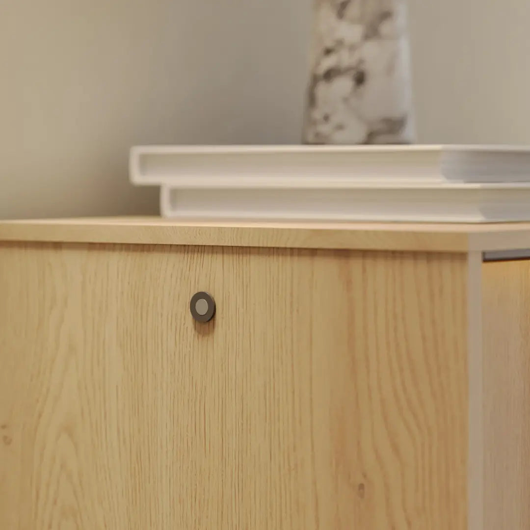 Wooden cabinet with a white shelf above it against a neutral wall.