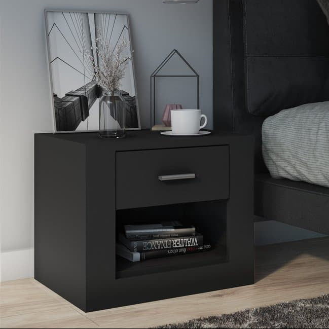 Black nightstand next to a bed with gray bedding and pillows.