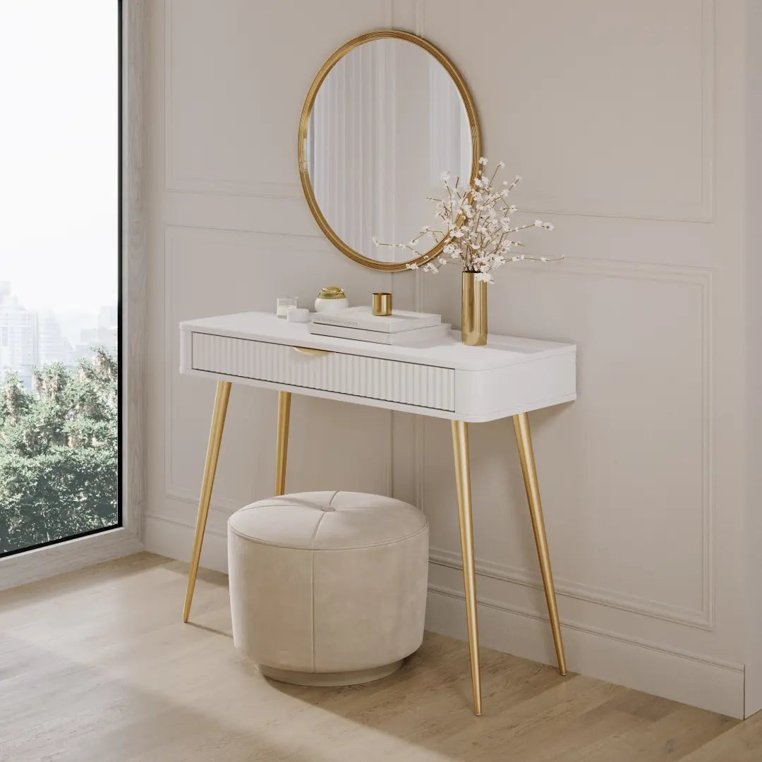 White vanity table with gold legs and mirror in a room with a window.
