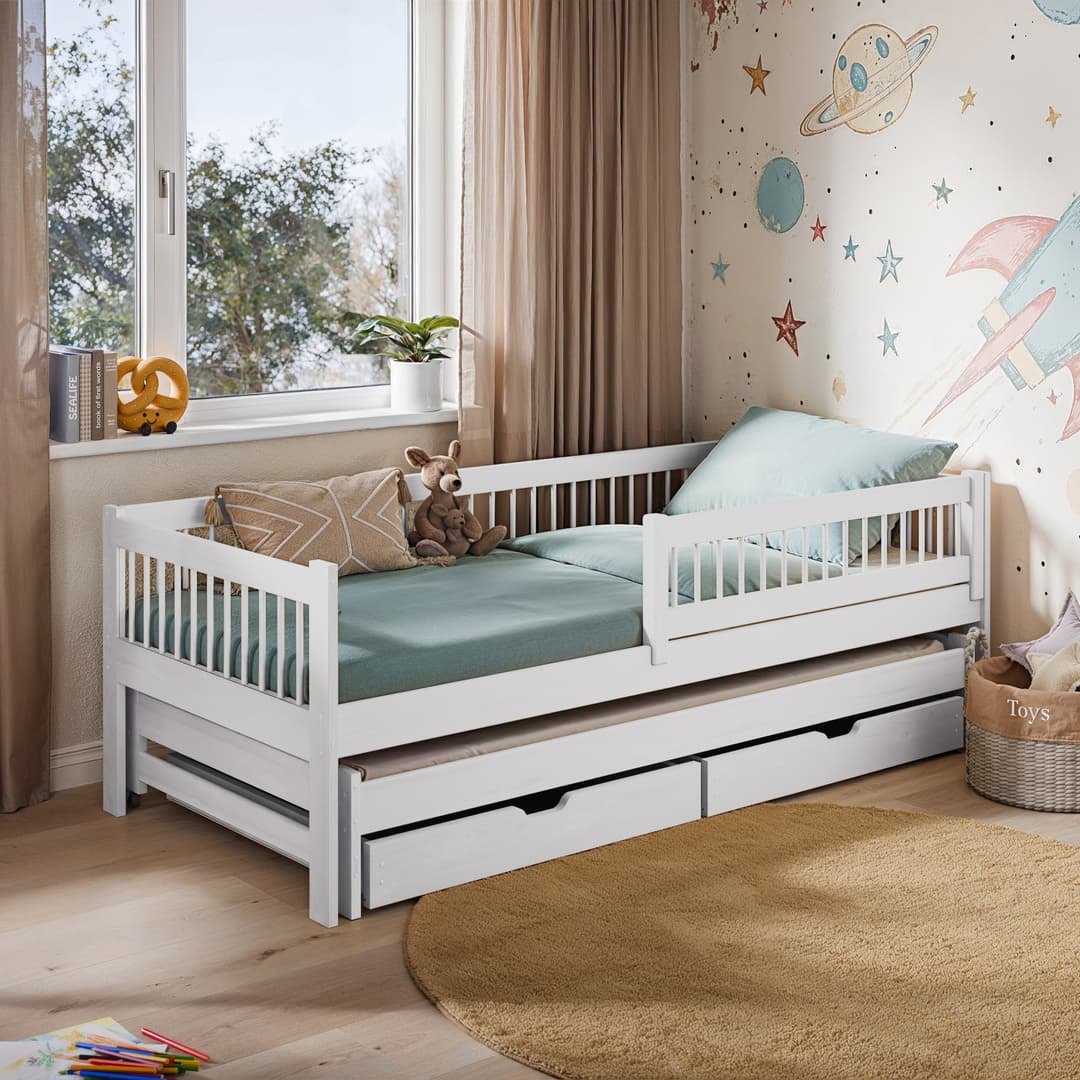 White children's bed with green mattress and trundle in a room with space-themed wallpaper.