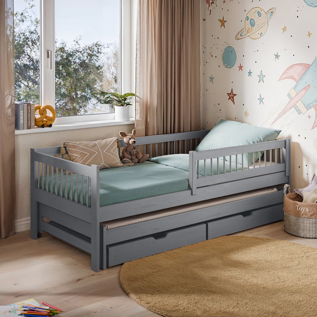 Children's bedroom with a gray bed and trundle, toys, and space-themed wallpaper.