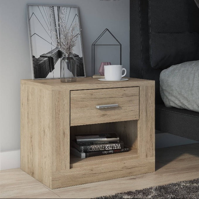 Wooden nightstand next to a bed with gray bedding and pillows.